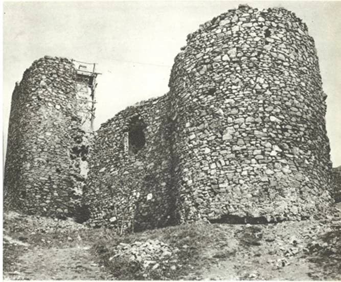 Stone ruins of Žrnov fortress with two cylindrical towers, partial collapse, and scaffolding on one tower, set on rocky terrain.