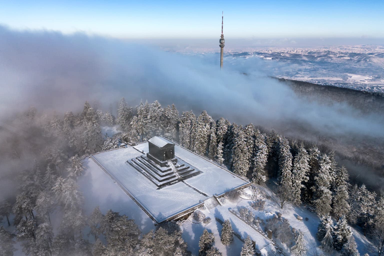Aerial view of Avala Tower and Monument to the Unknown Hero covered in snow with snow-laden trees and fog in the background