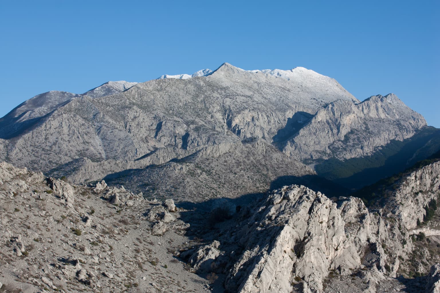 Mountain range with rocky terrain and snow-covered peaks under clear blue sky