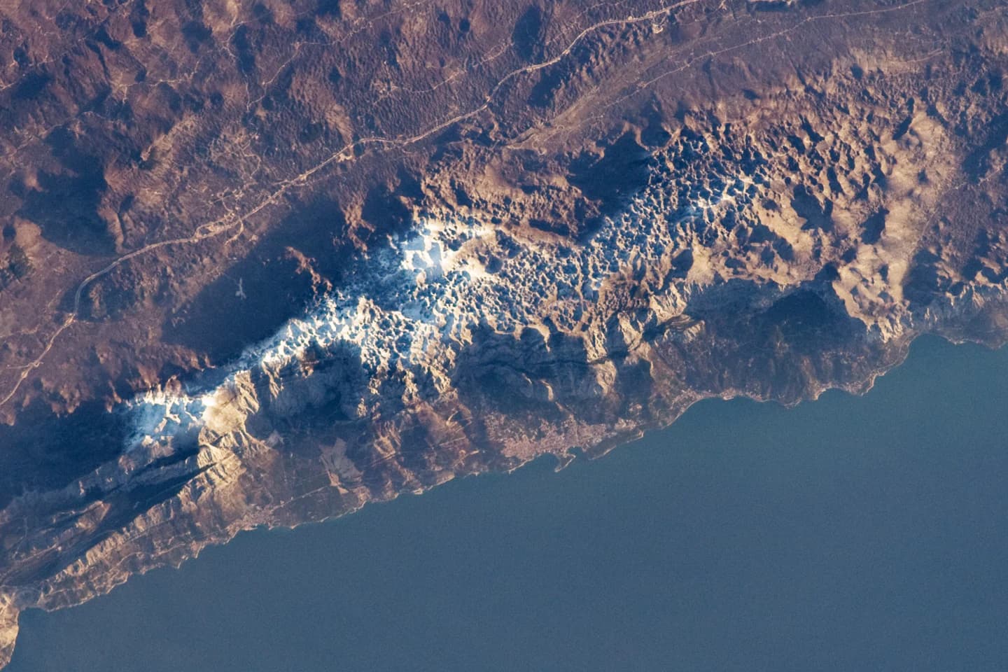 Satellite view of coastal mountain range with patches of snow or ice along the ridge
