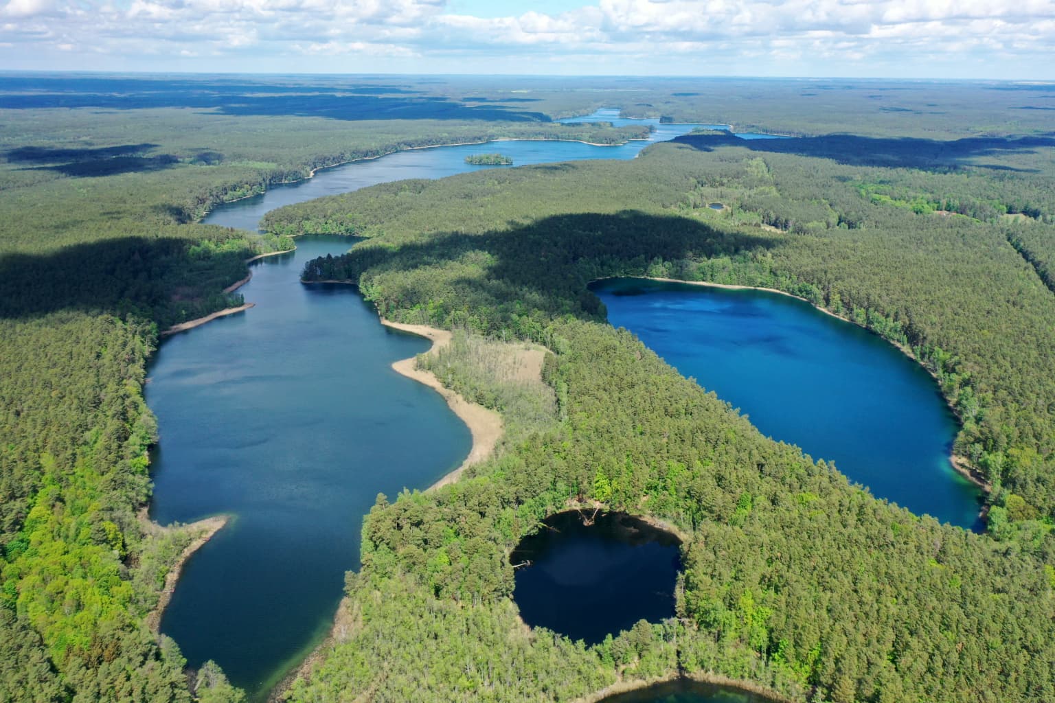 Aerial view of two blue lakes surrounded by dense green forest with a smaller lake in the foreground