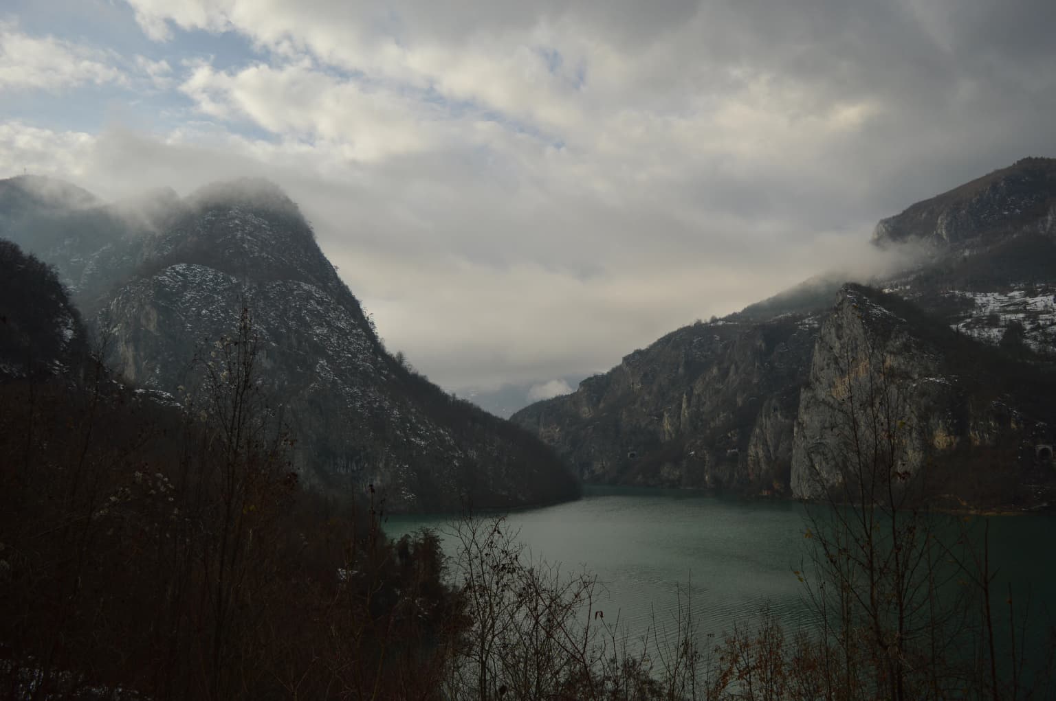 Mountainous landscape featuring a body of water with misty peaks and forested slopes