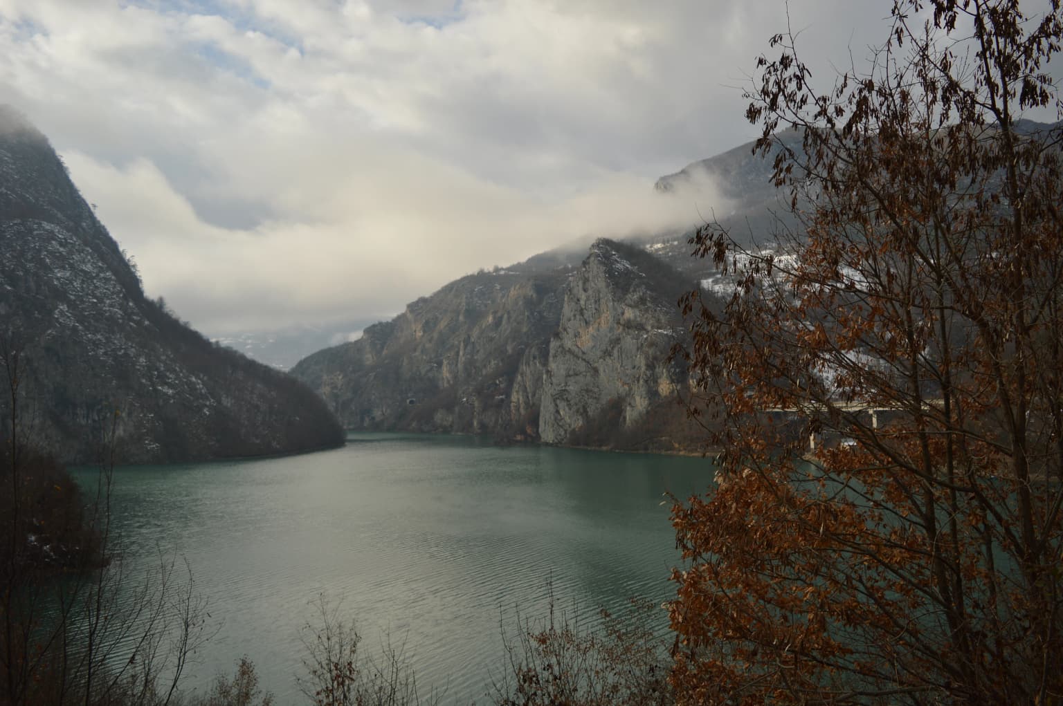 Mountain lake surrounded by rocky hills and autumn trees under a cloudy sky