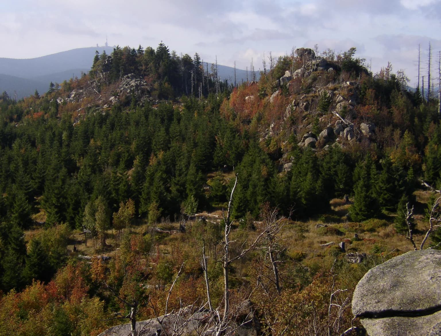 Landscape view showing forested hills, rocky formations, and distant mountains under a partly cloudy sky