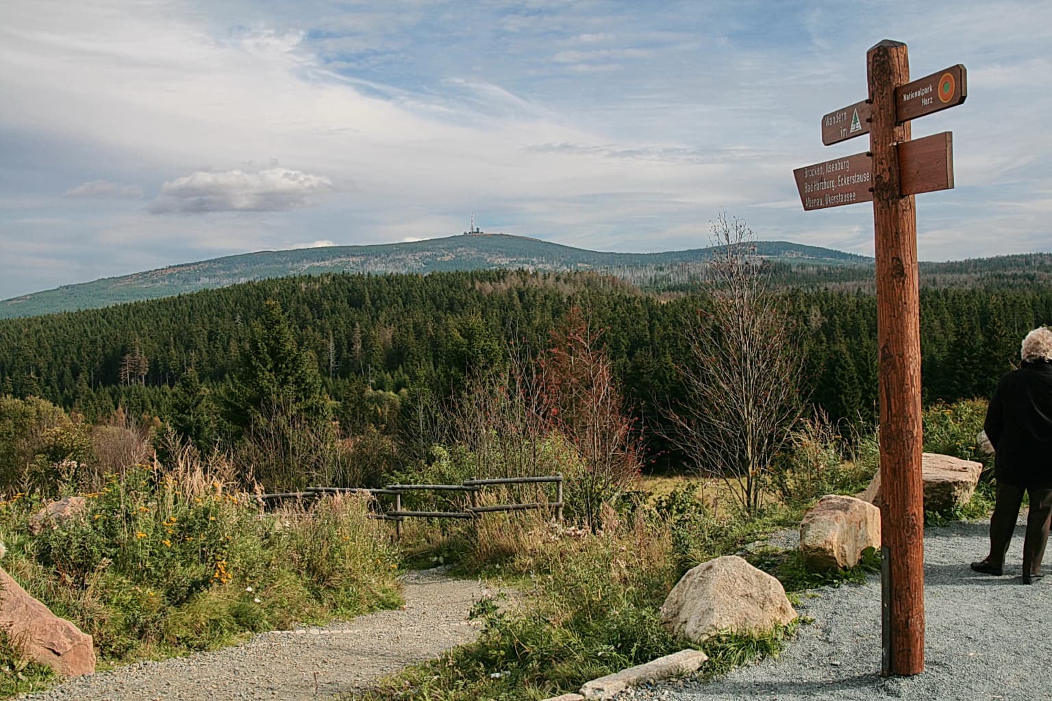 Wooden signpost with directional signs at a gravel overlook with forested mountains in the background