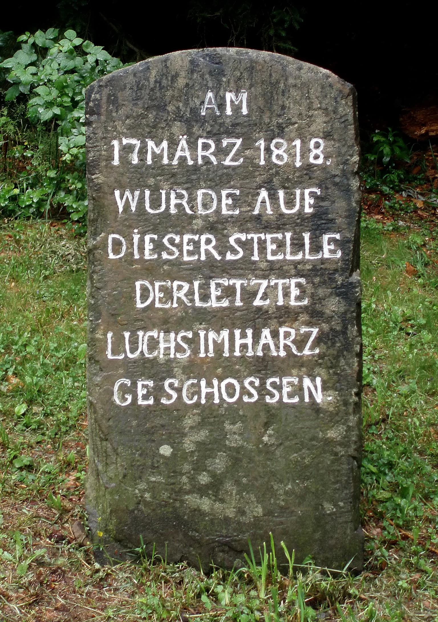 Weathered stone monument with white carved German text in a grassy natural setting