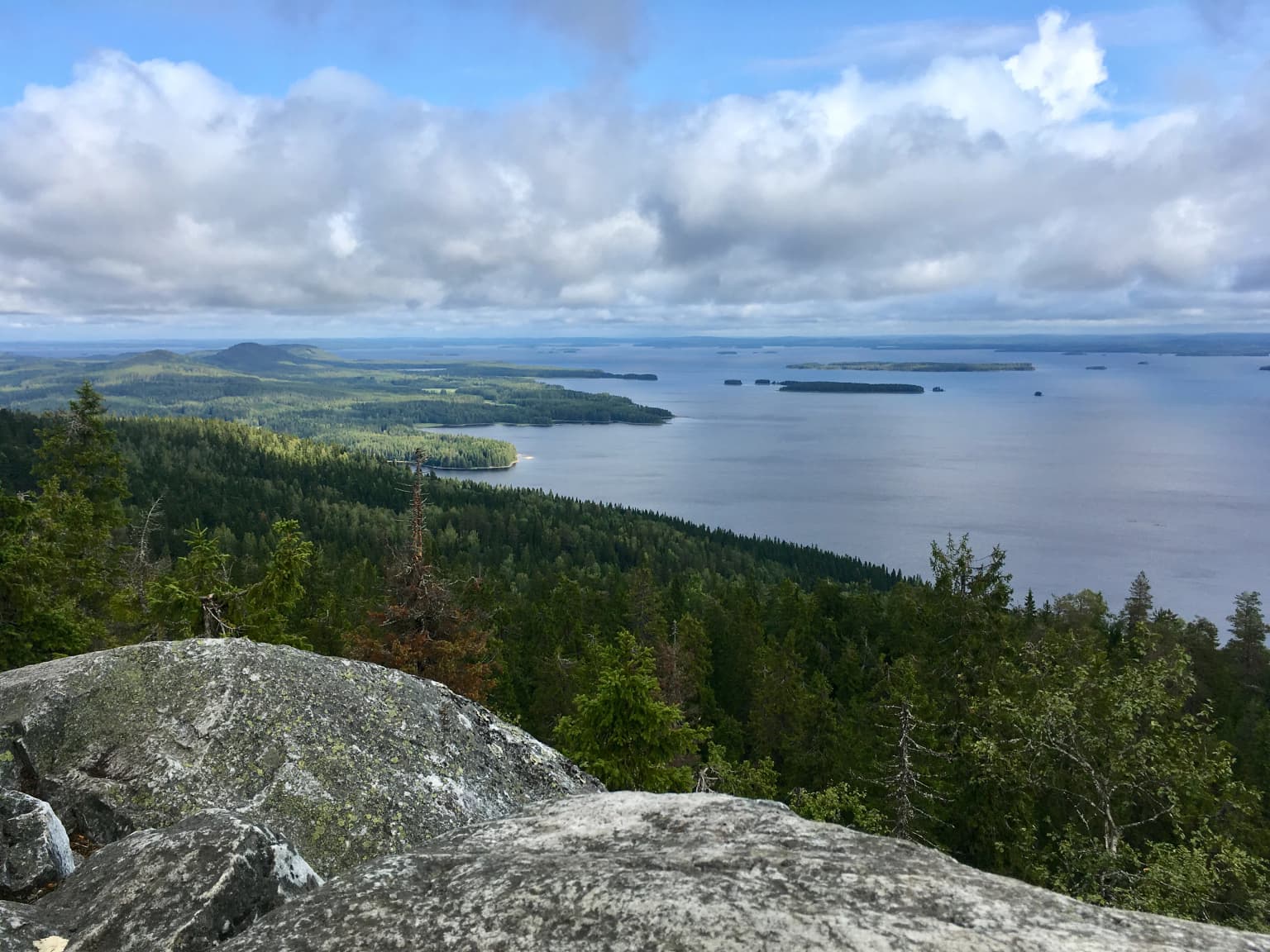 Panoramic view of Lake Pielinen surrounded by forested hills under a partly cloudy sky