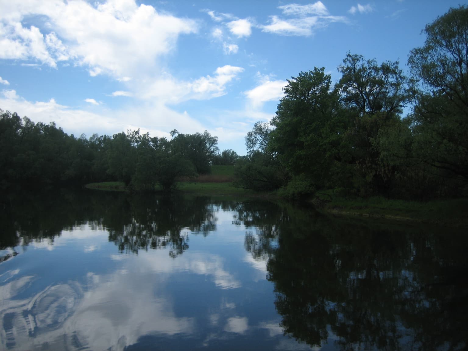 Calm lake reflecting blue sky with white clouds and surrounding green trees