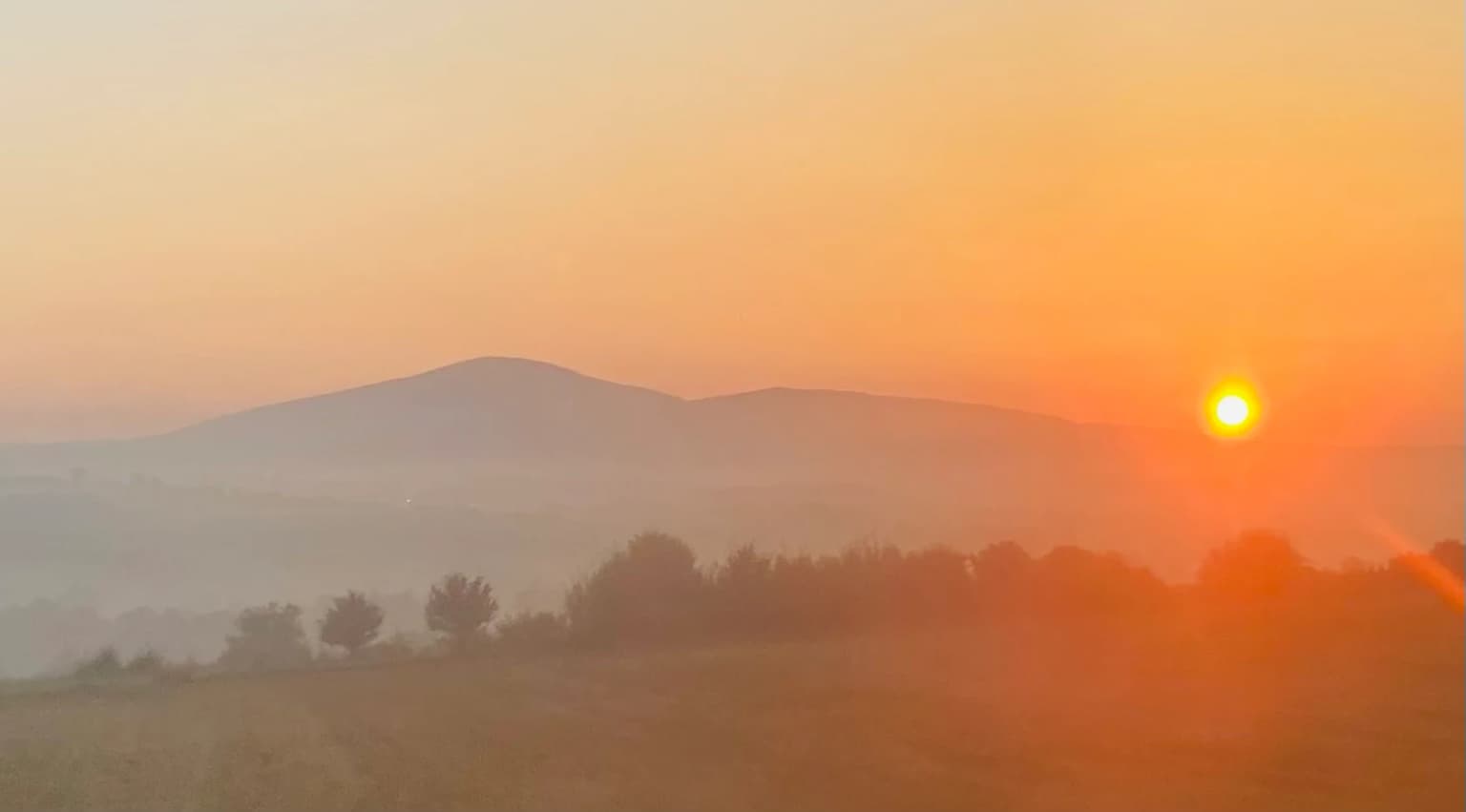 Sunrise over Kosmaj mountain with misty landscape and trees in the foreground