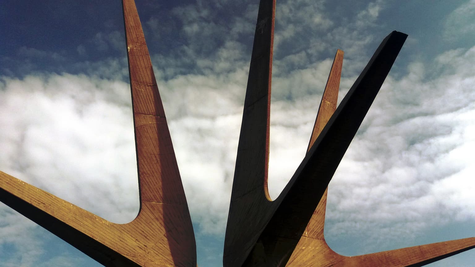 Close-up view of the Kosmaj Monument's angular wooden and metal beams against a partly cloudy sky