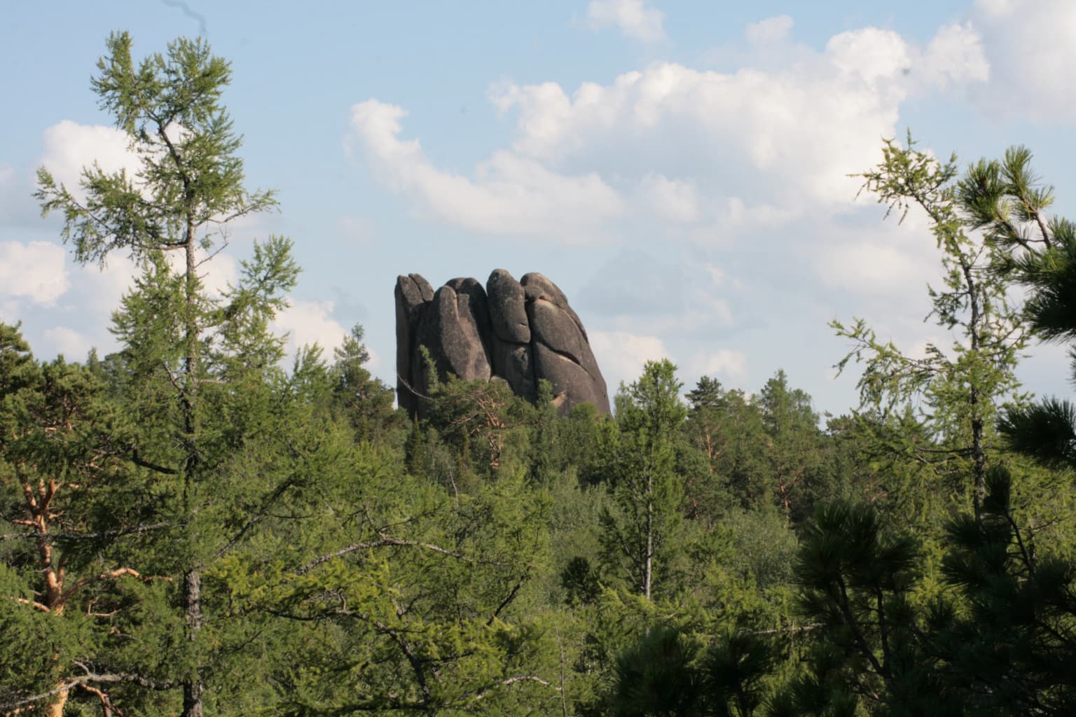 Tall dark rock formations rising above dense green forest under a partly cloudy sky