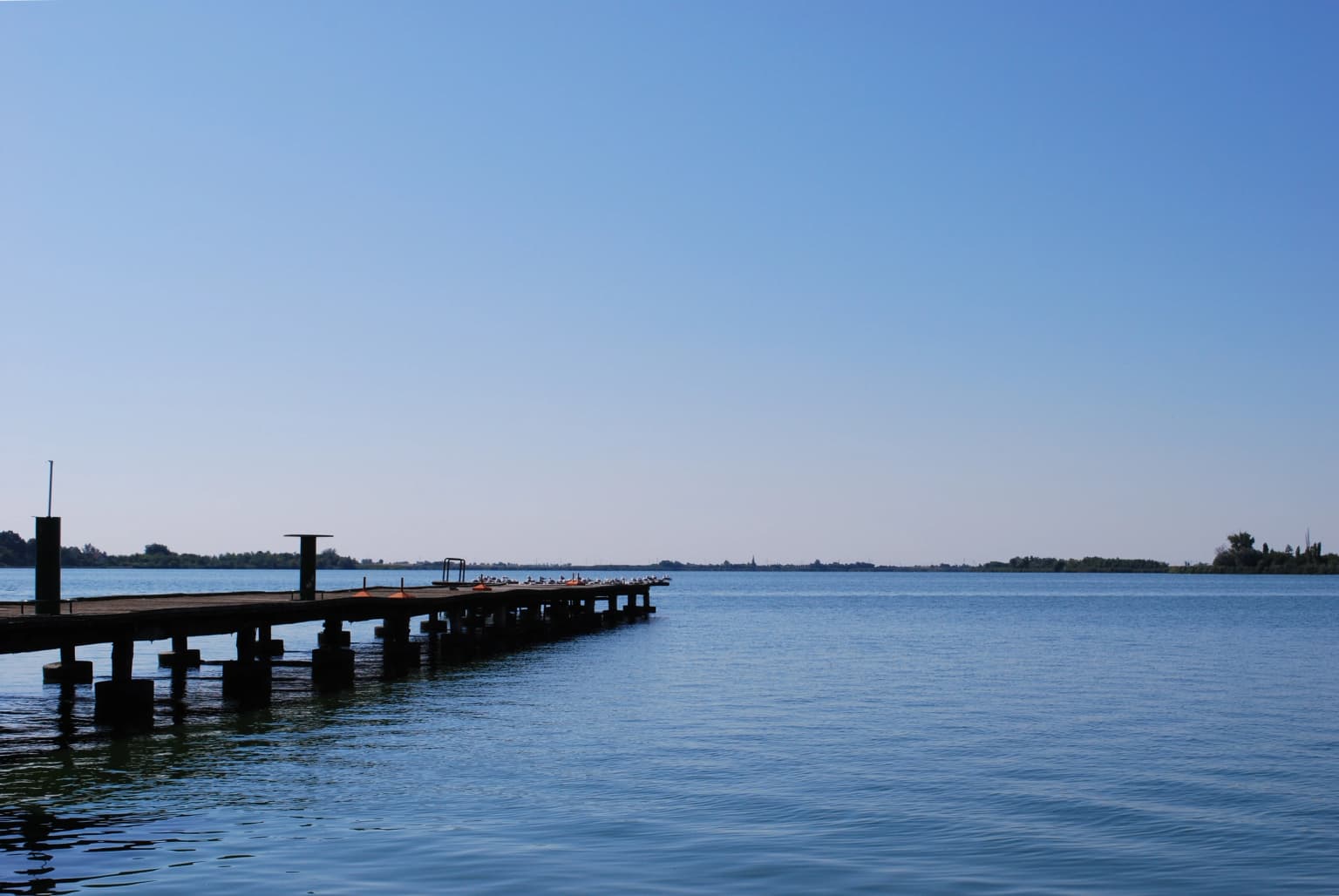 Calm lake with a wooden pier extending into the water under a clear blue sky