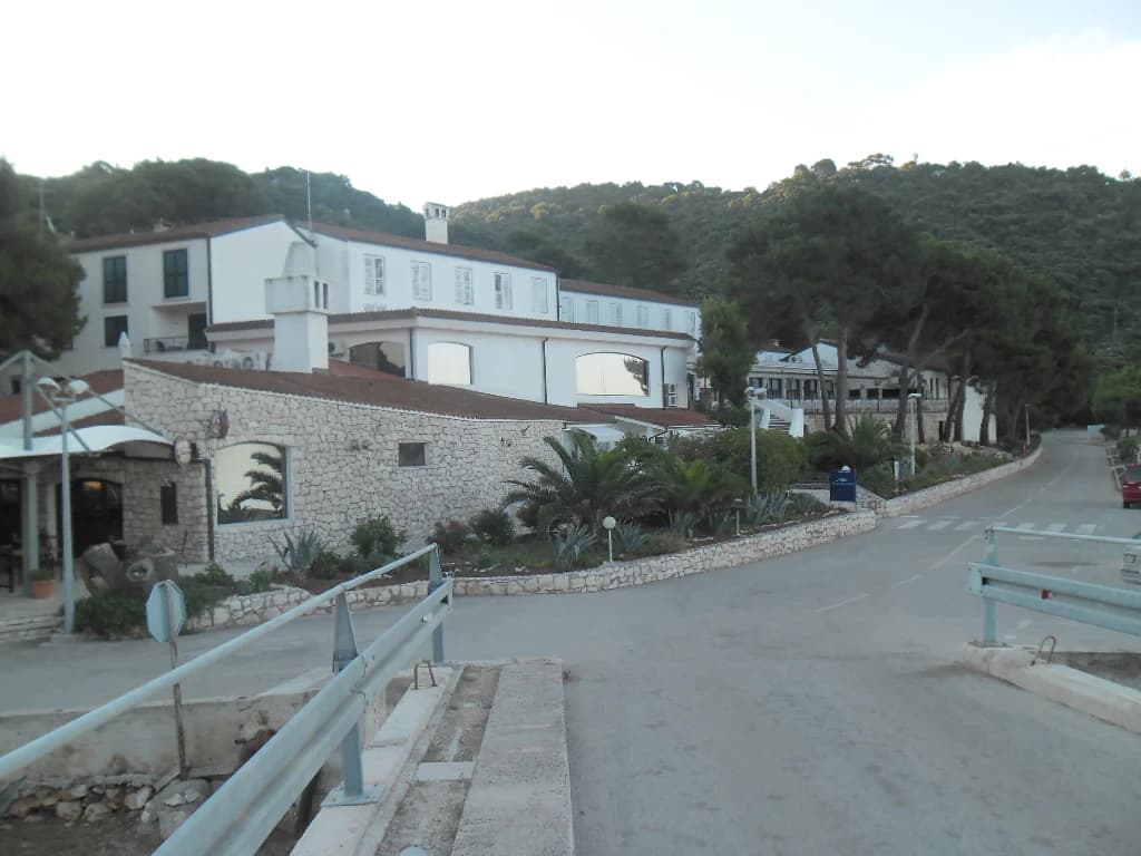 Stone and white building with red roof, surrounded by trees and a paved road with guardrails on Lastovo Island
