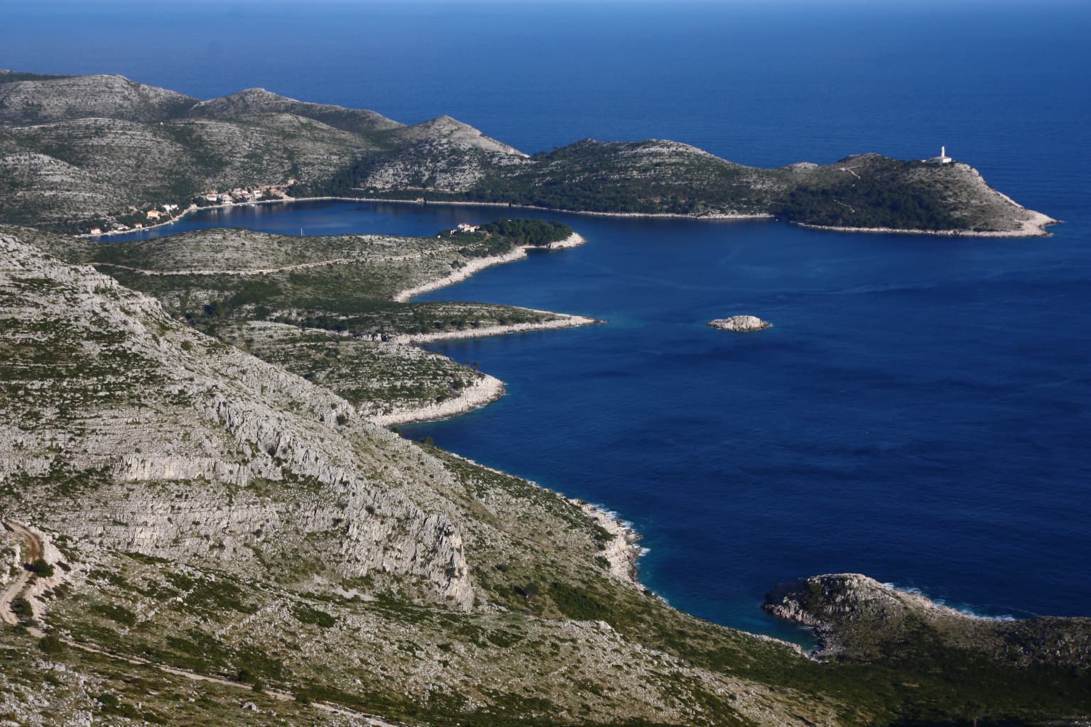 Coastal bay with rocky islands, deep blue sea, and mountainous coastline under clear sky