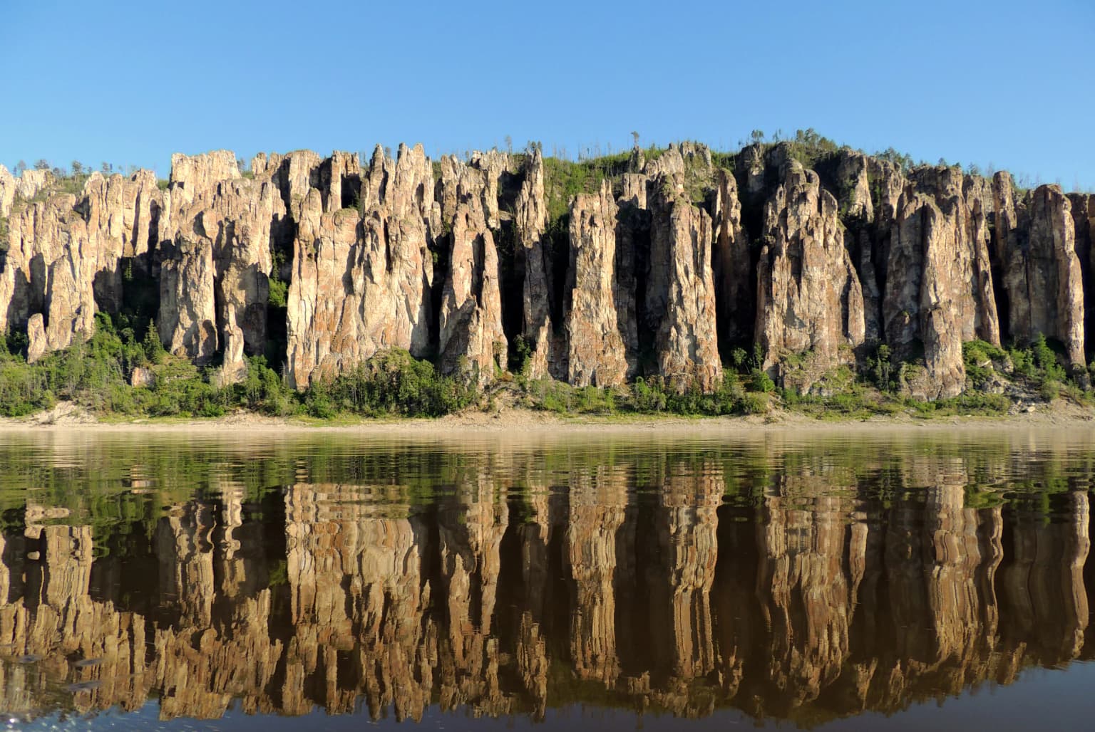 Tall rock pillars reflecting in a river under a clear blue sky
