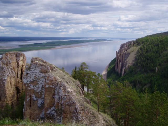 Rock formations along the Lena River with forested hills under a partly cloudy sky
