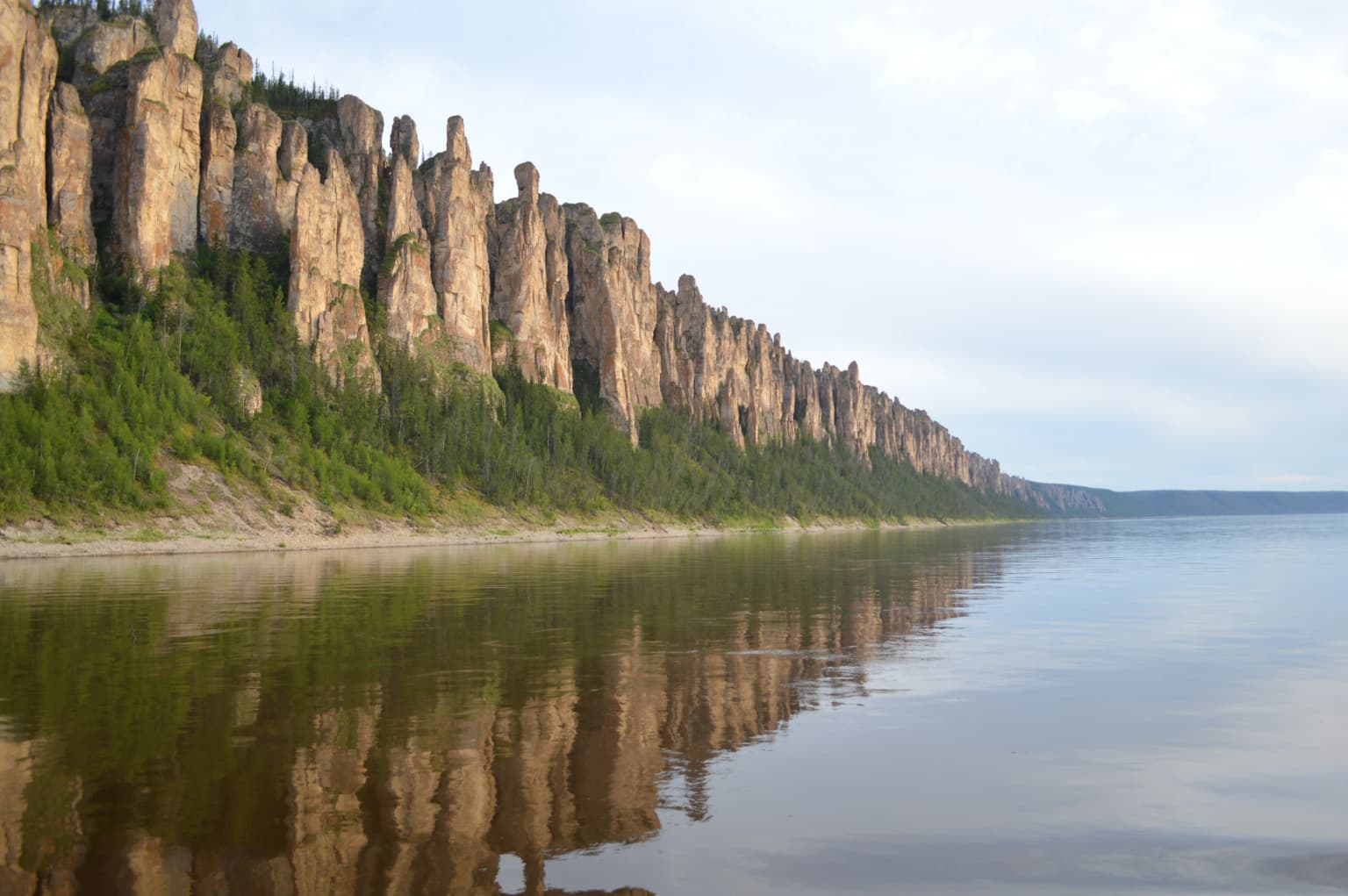 A river with calm water reflecting tall rock formations along the shoreline