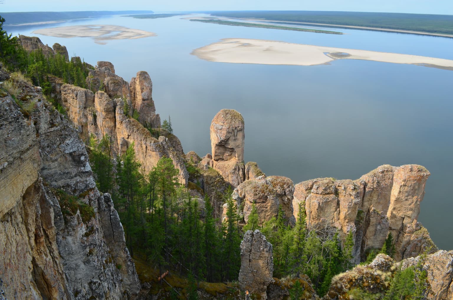 Rock pillars rising from forested riverbank, with Lena River and sandbars in the background