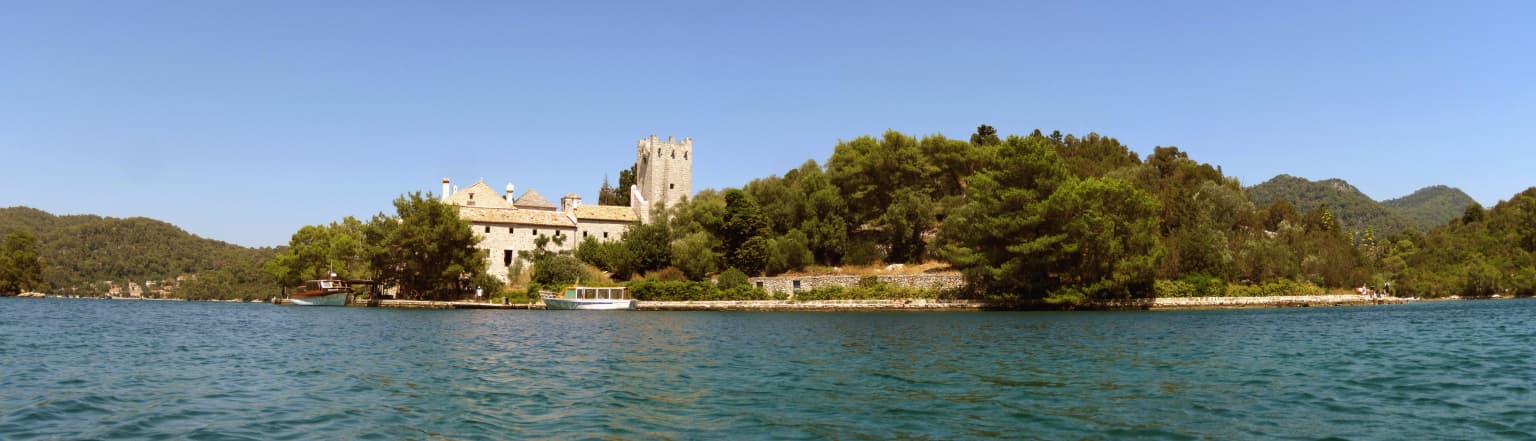 Wide view of Veliko jezero lake with St. Mary's Island, a historic monastery, and surrounding greenery under clear blue sky