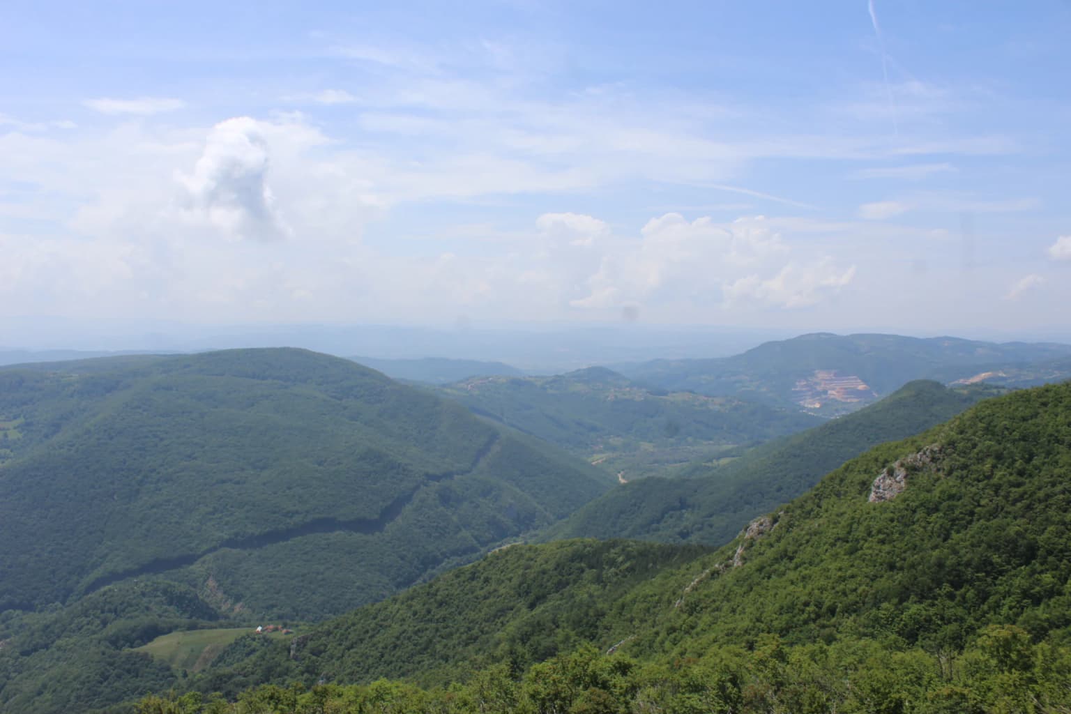 Wide view of mountainous landscape with lush green forests, valleys, and rolling hills under a partly cloudy sky