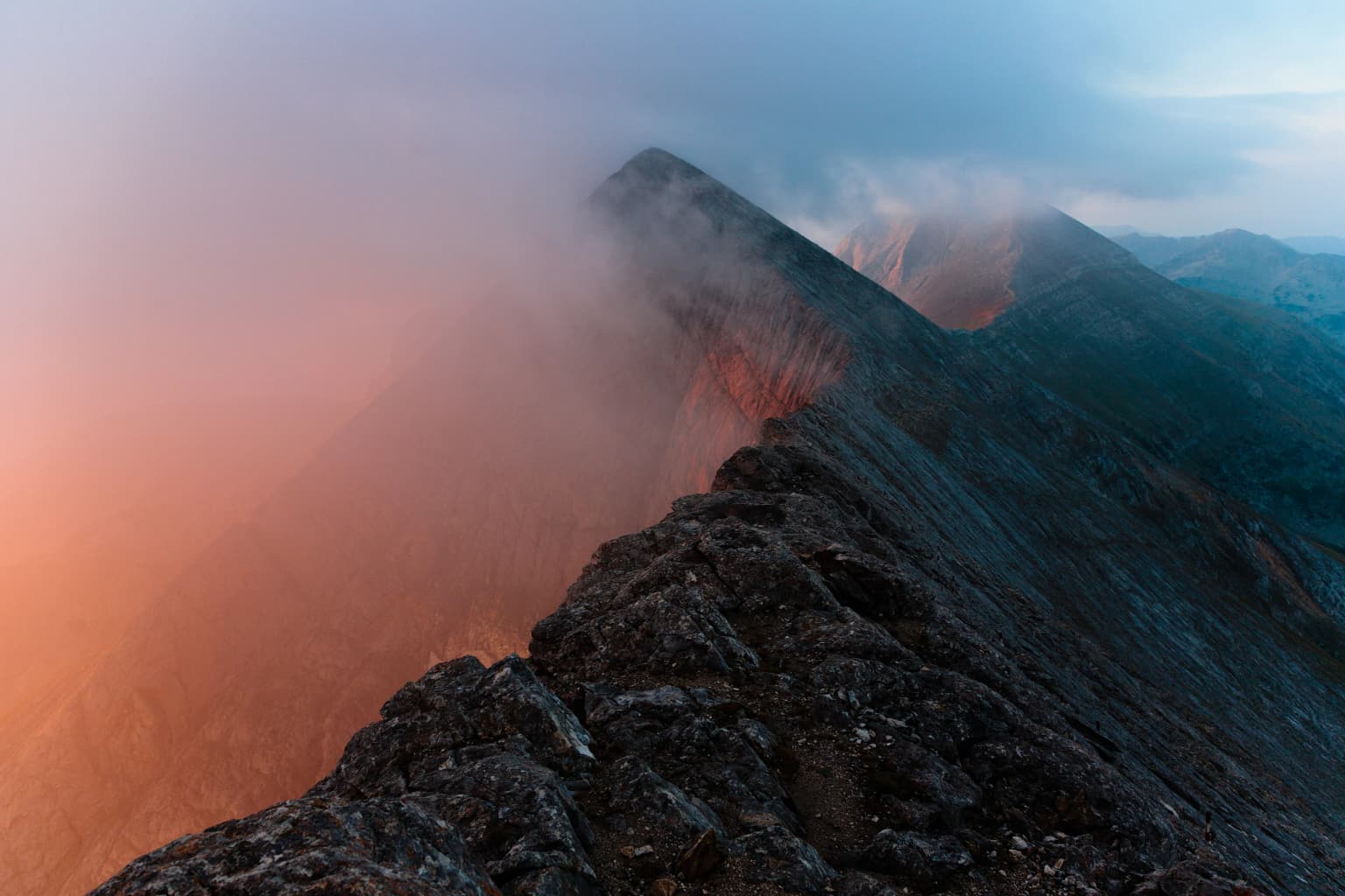 Rocky mountain peak with mist, illuminated by orange dawn light against a cloudy sky