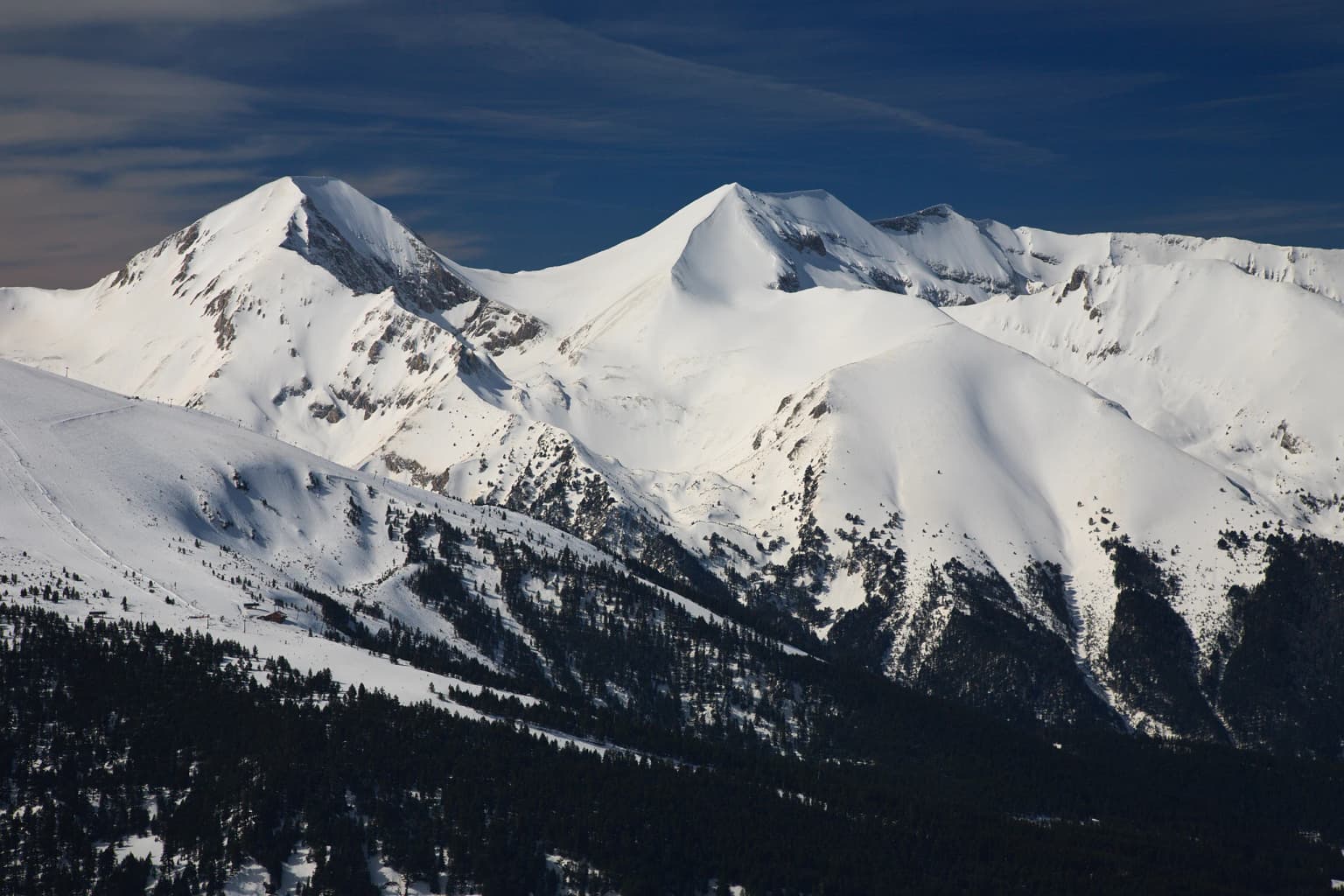 Snow-covered mountain peaks with dark forested slopes beneath a clear blue sky