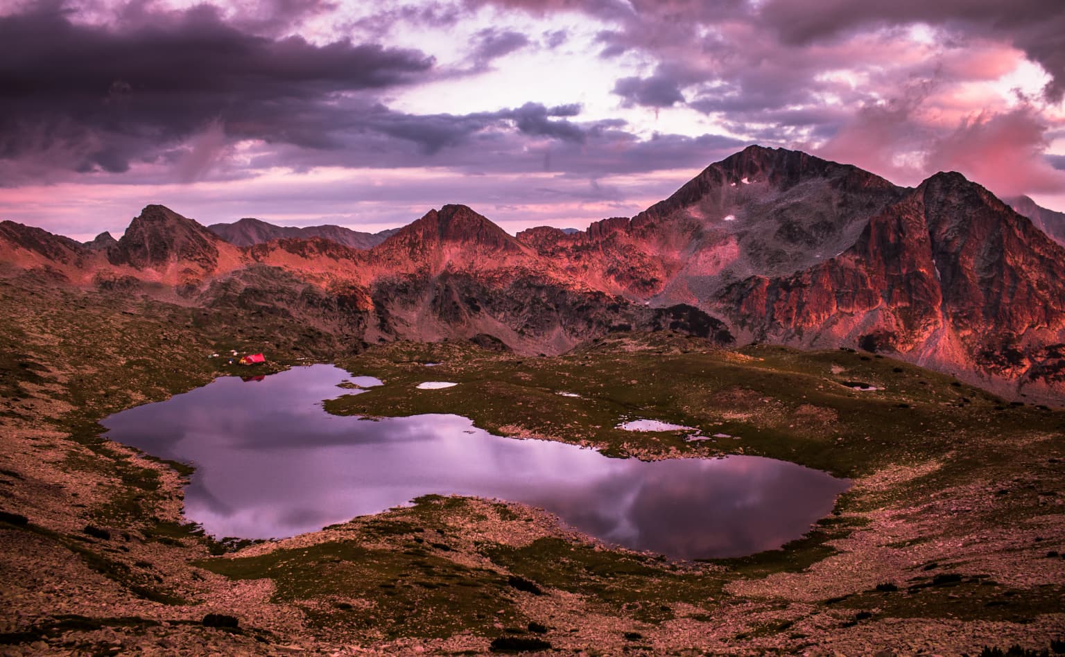 A lake surrounded by mountains at sunset with pink and purple clouds in the sky