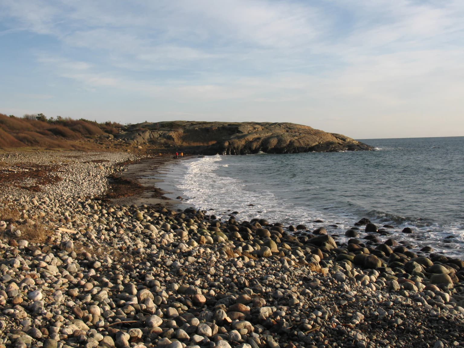 Rocky beach with waves crashing against shore, showing coastal landscape with hills in background