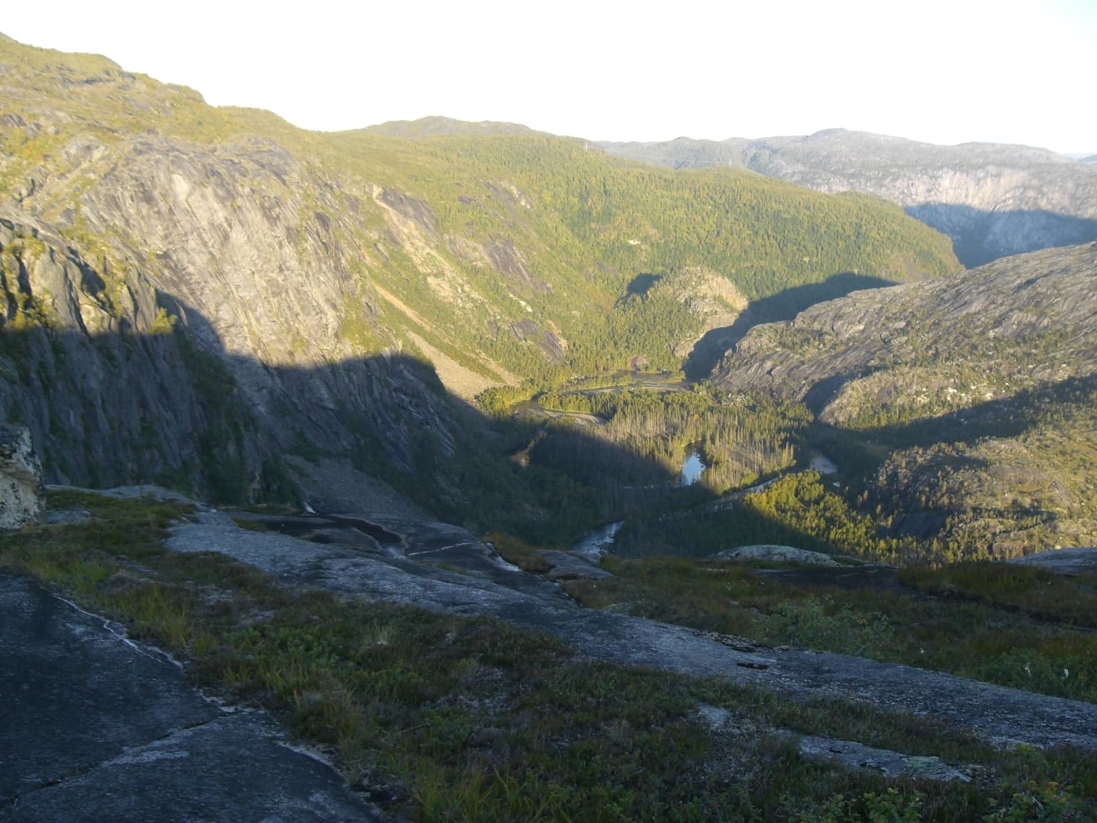 Mountainous valley with river, green slopes, and rocky terrain at sunset