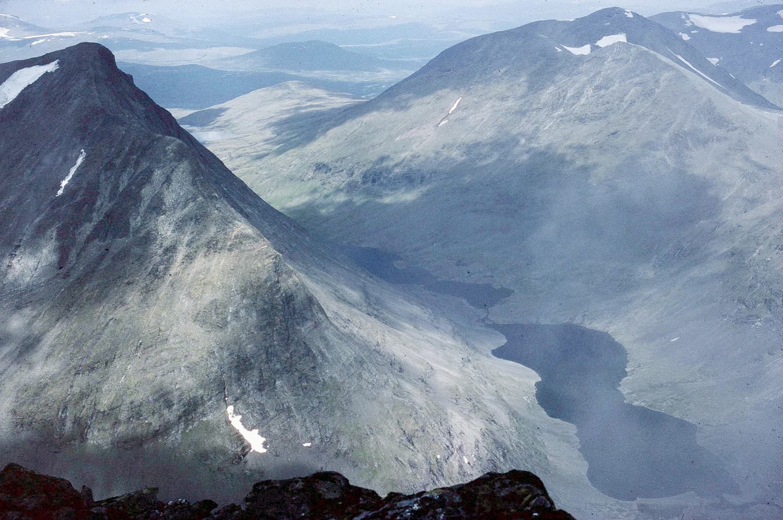 Mountainous landscape with rocky peaks, snow patches, valley, and lake in Sarek National Park