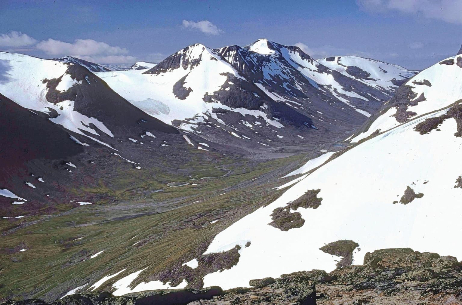 Snow-capped mountain peaks with patches of green vegetation in a valley, showing the alpine landscape of Sarek National Park