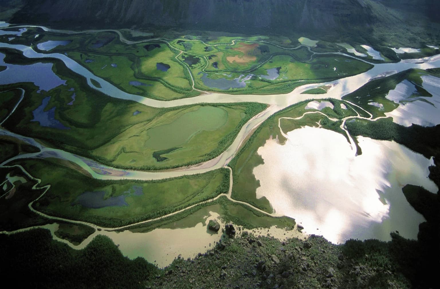 Aerial photograph of a river delta with winding waterways, green valleys, and mountainous terrain in Sarek National Park