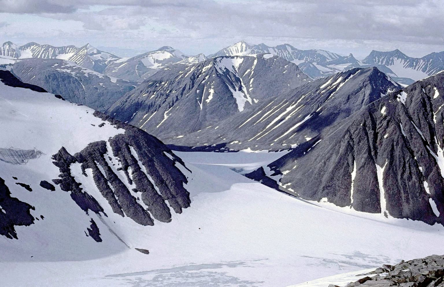 Snow-covered mountain peaks with glaciers and rocky ridges under a partly cloudy sky