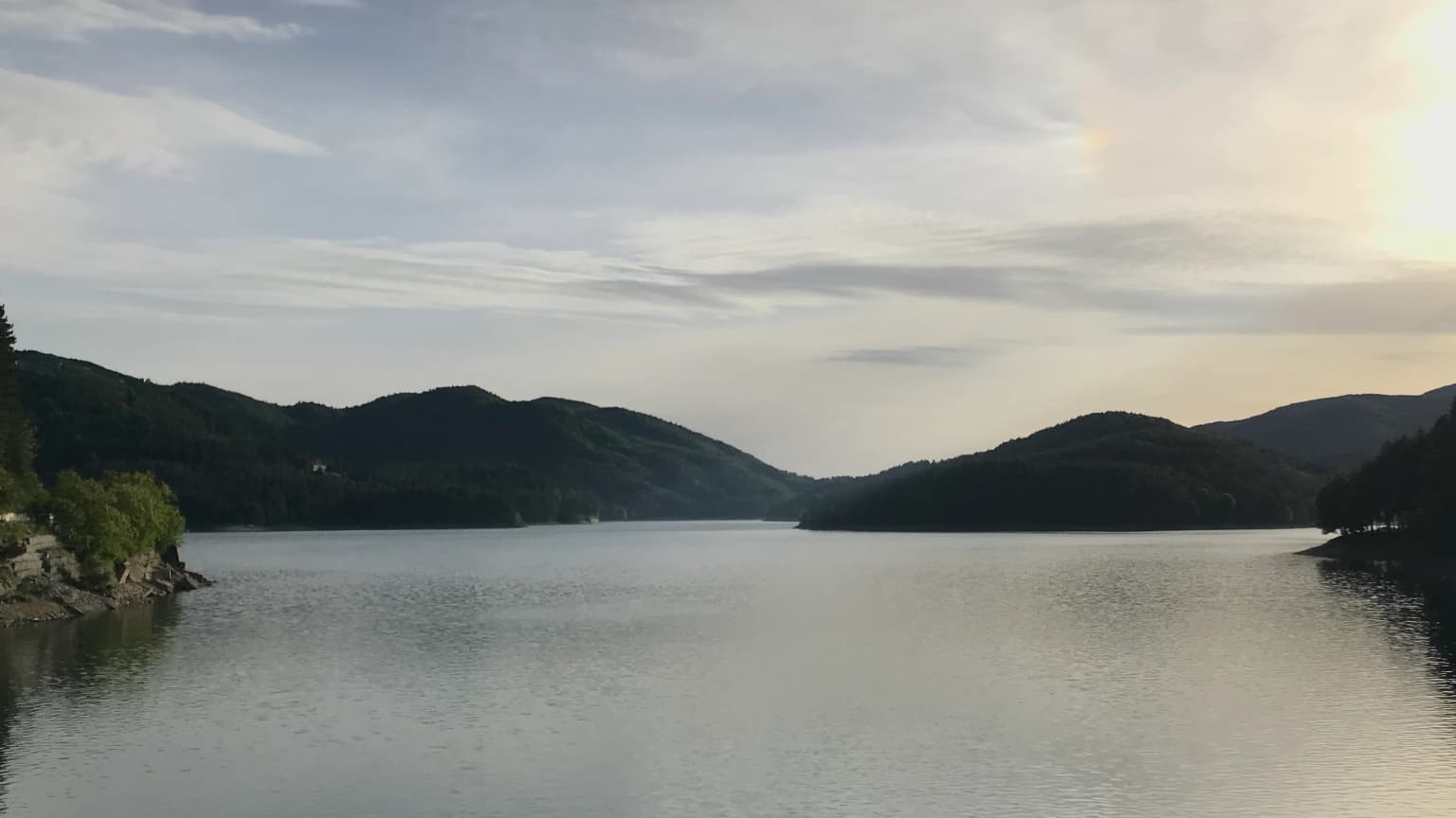 Calm lake surrounded by rolling hills under a partly cloudy sky