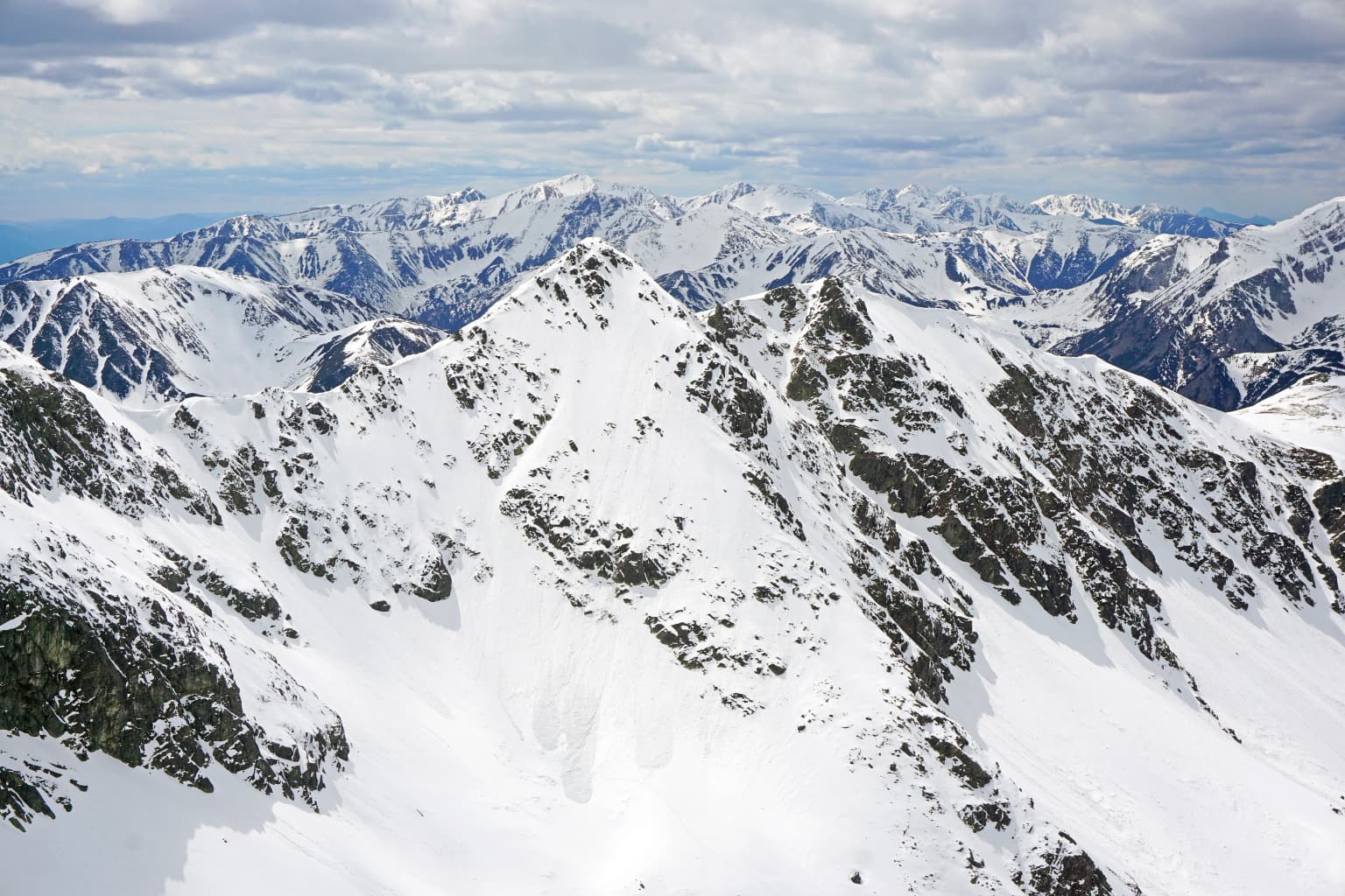 Snow-covered mountain peaks with rocky outcrops under a partly cloudy sky