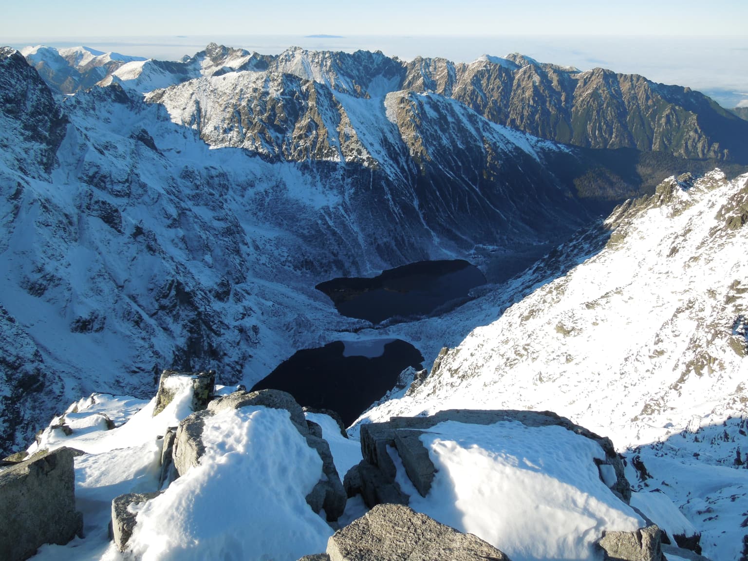Snowy mountain peaks with a valley and lake in the background