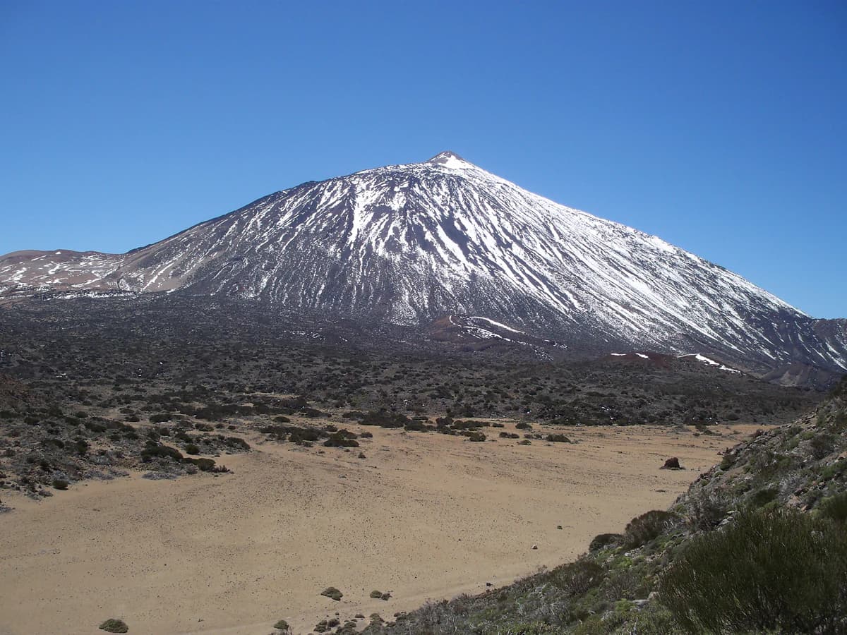 Wide view of Mount Teide with snow-capped peak against clear blue sky, showing volcanic landscape below