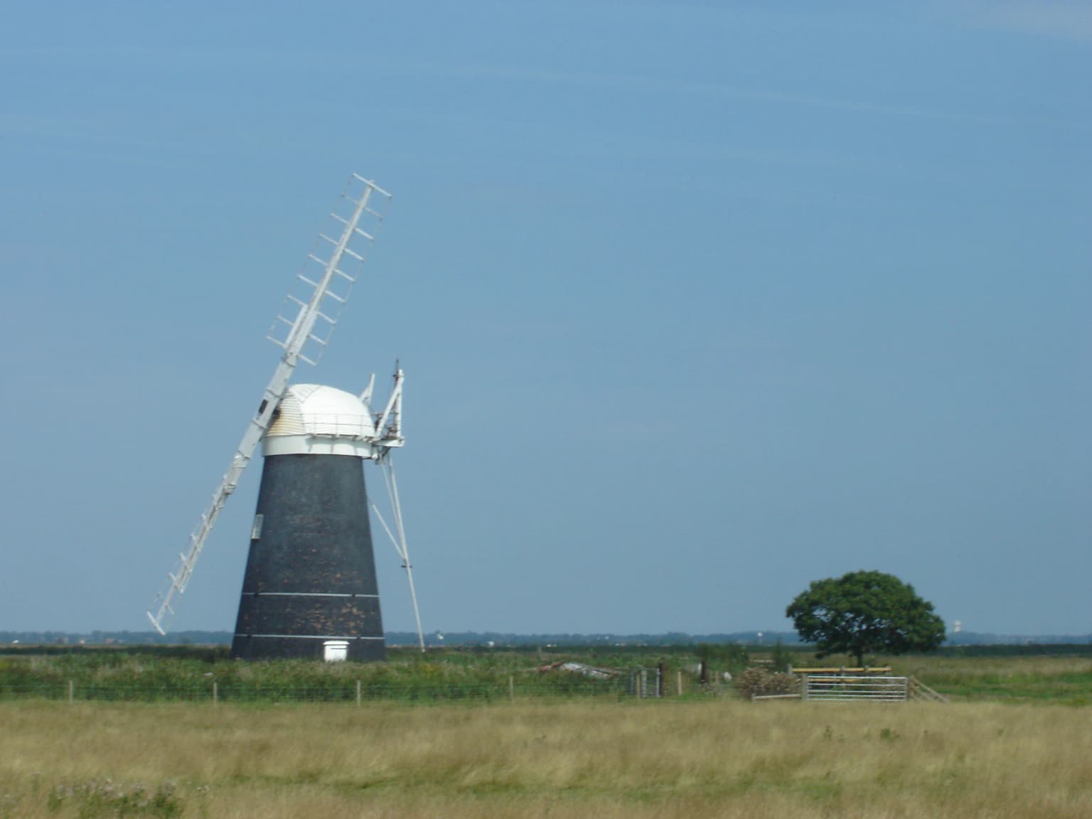 Black and white windmill with a large propeller in a grassy field under a clear blue sky