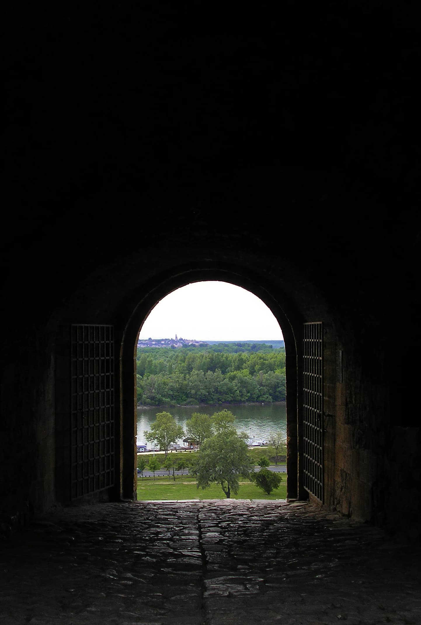 Stone archway with metal grilles framing a view of a forested island across a river