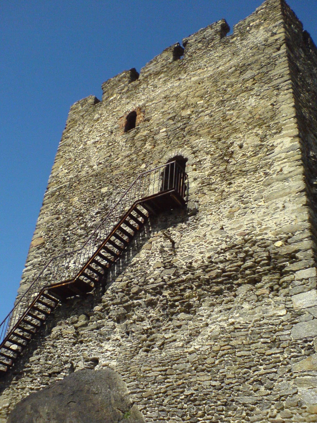 Stone tower with metal staircase and small window under clear blue sky.