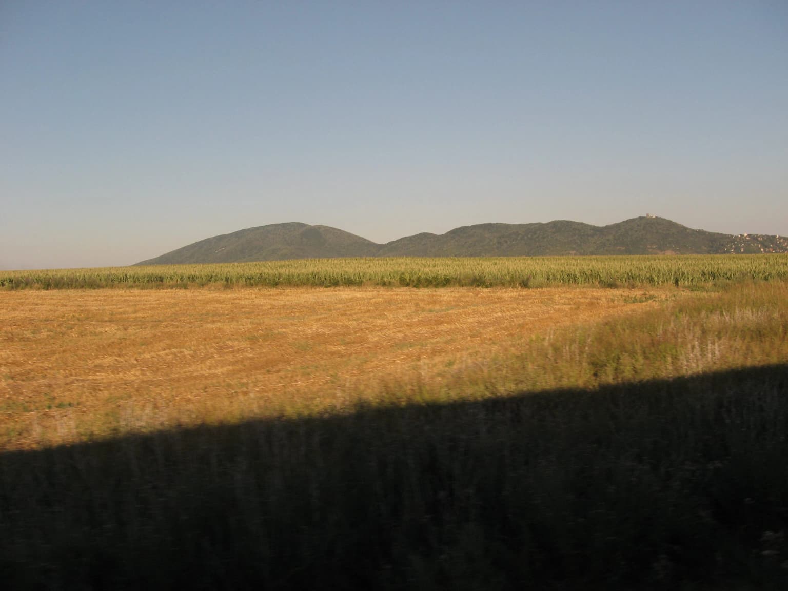 A landscape view of the Vršac Mountains with a large field in the foreground and distant hills under a clear blue sky