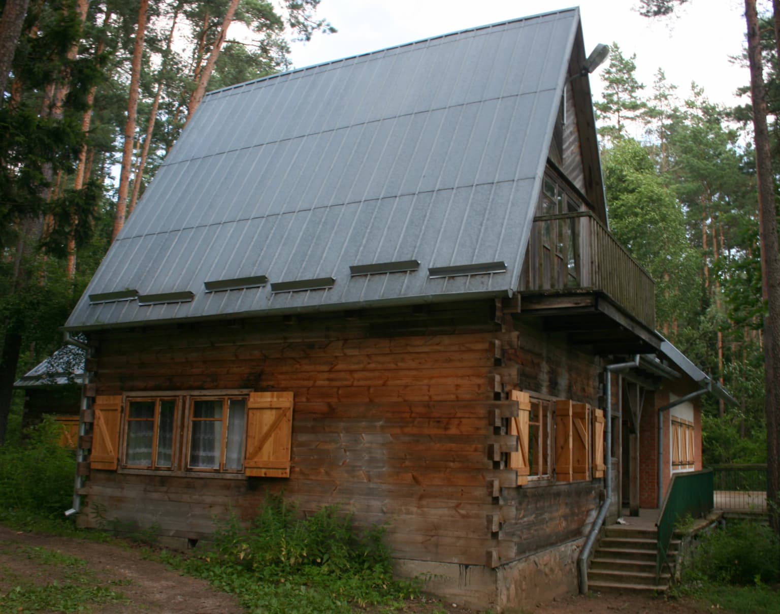 Wooden building with metal roof and wooden shutters, surrounded by forest, with staircase leading to entrance