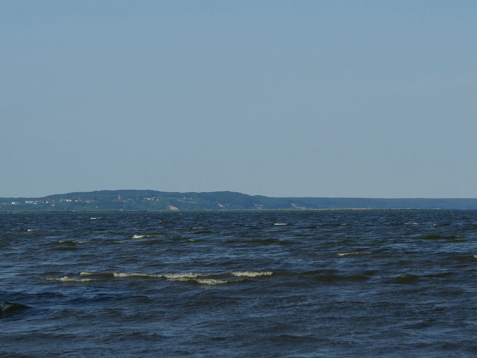 Wide view of the sea with distant shoreline and hills under a clear sky