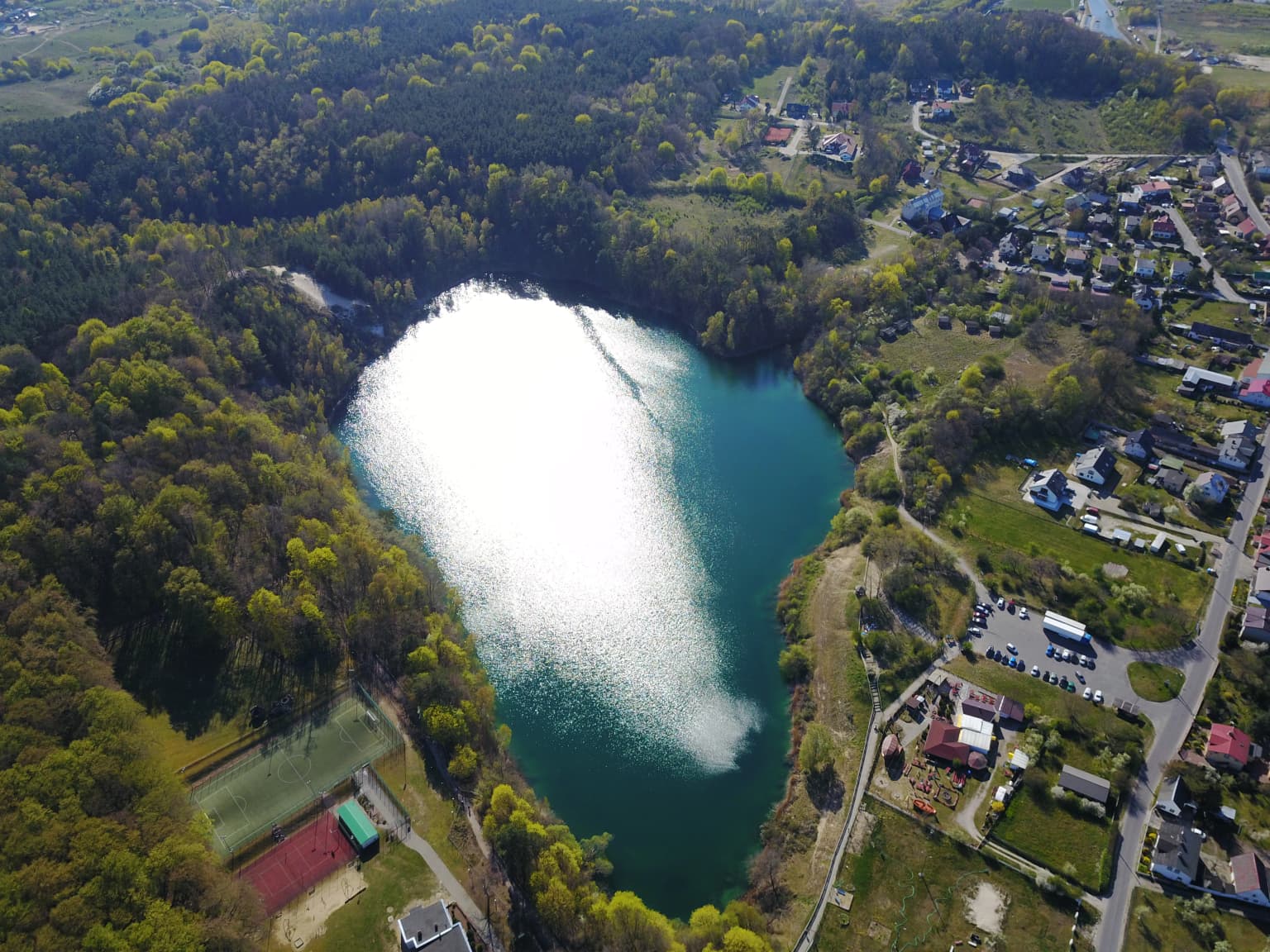 Aerial view of a turquoise lake surrounded by forested hills with adjacent roads and buildings