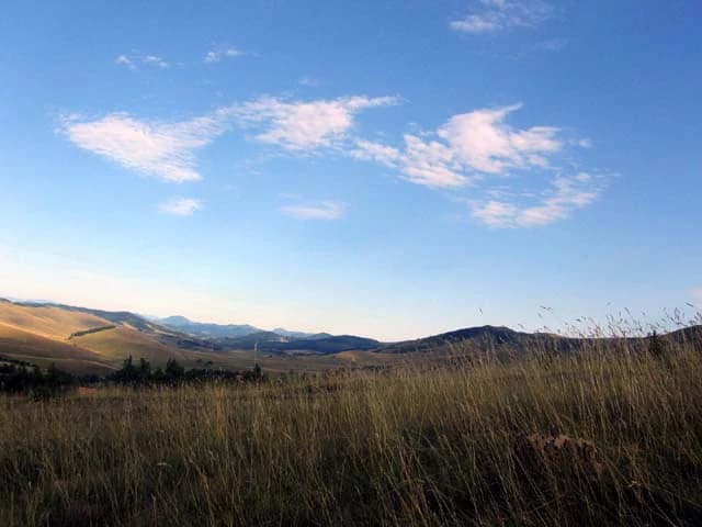 Open grassy field with rolling hills under a blue sky with scattered clouds