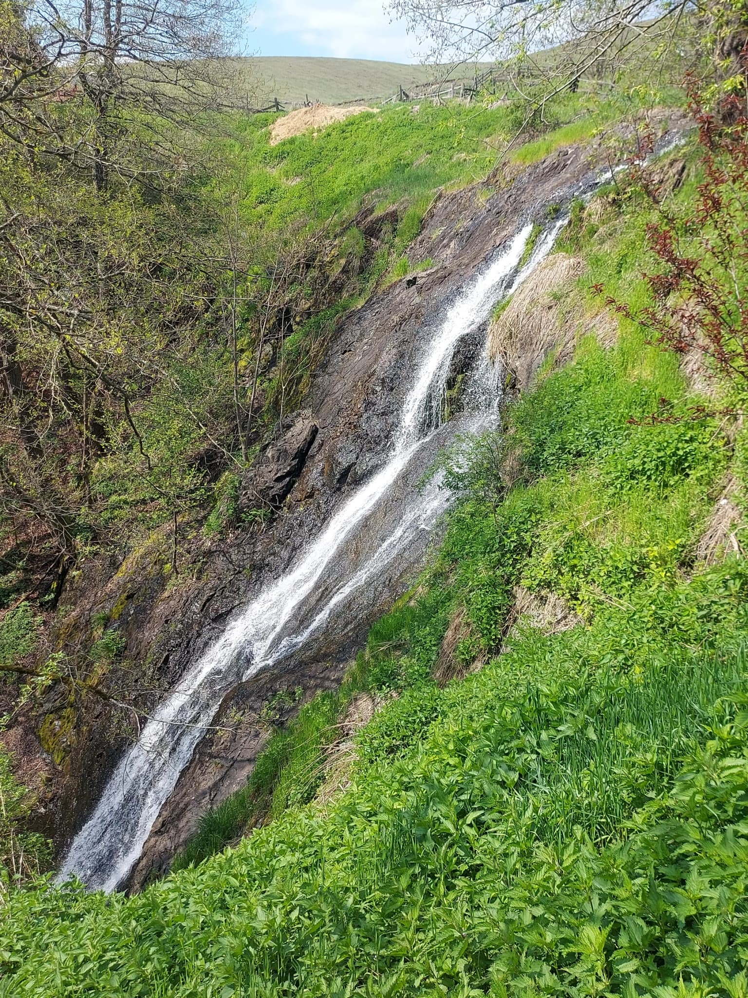 Waterfall cascading down rocky terrain with greenery on both sides