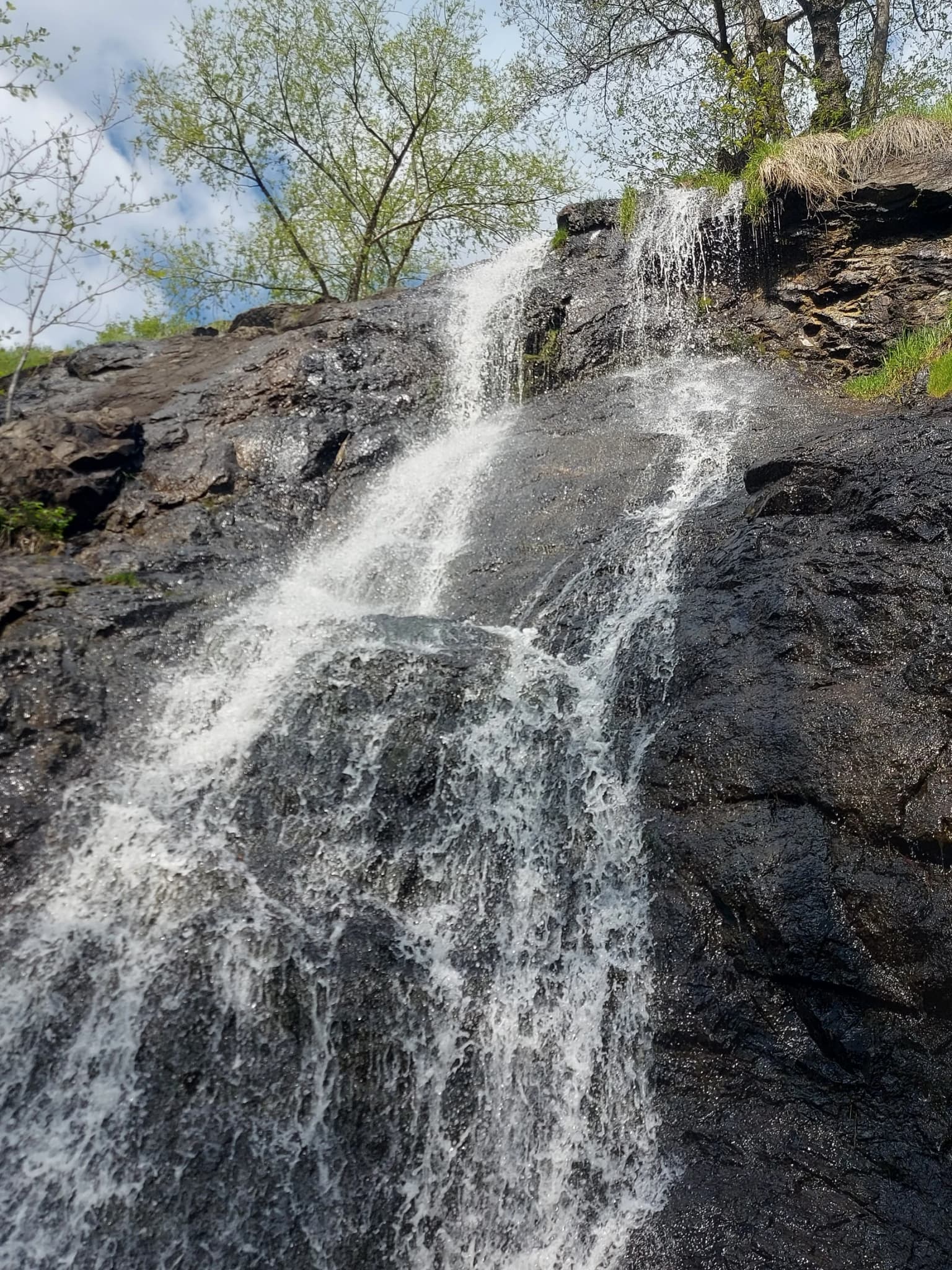 Waterfall flowing down dark rocks with some vegetation and trees in background
