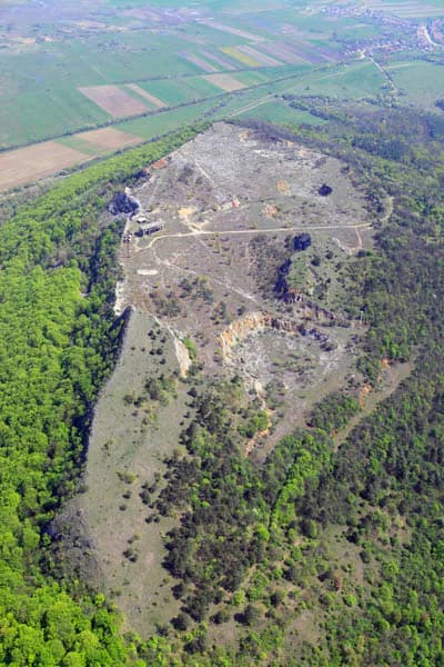Aerial view of Esztramos Hill surrounded by green forests and agricultural fields, with rocky terrain visible.