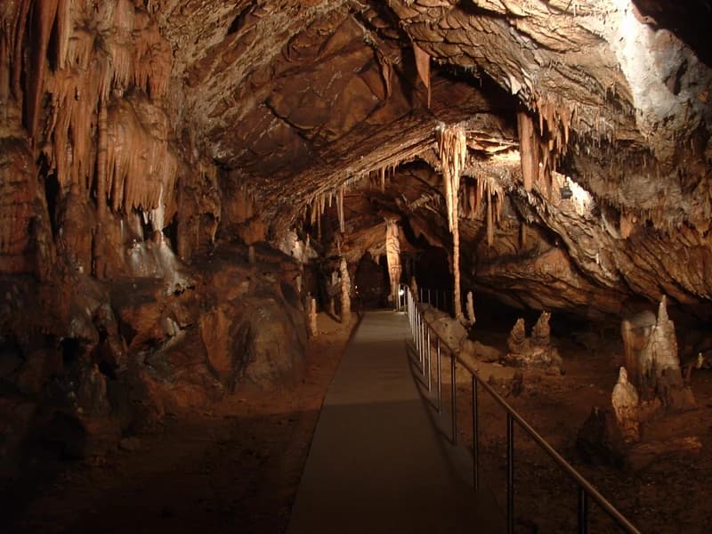 Stalactites hanging from cave ceiling, metal railing, stone pathway in Aggtelek National Park's Baradla Cave