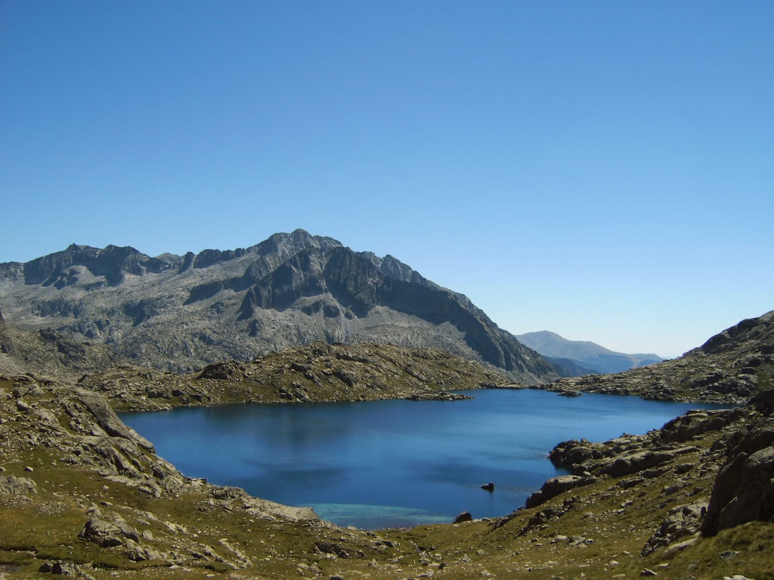 A clear blue lake surrounded by rocky mountain slopes under a bright blue sky
